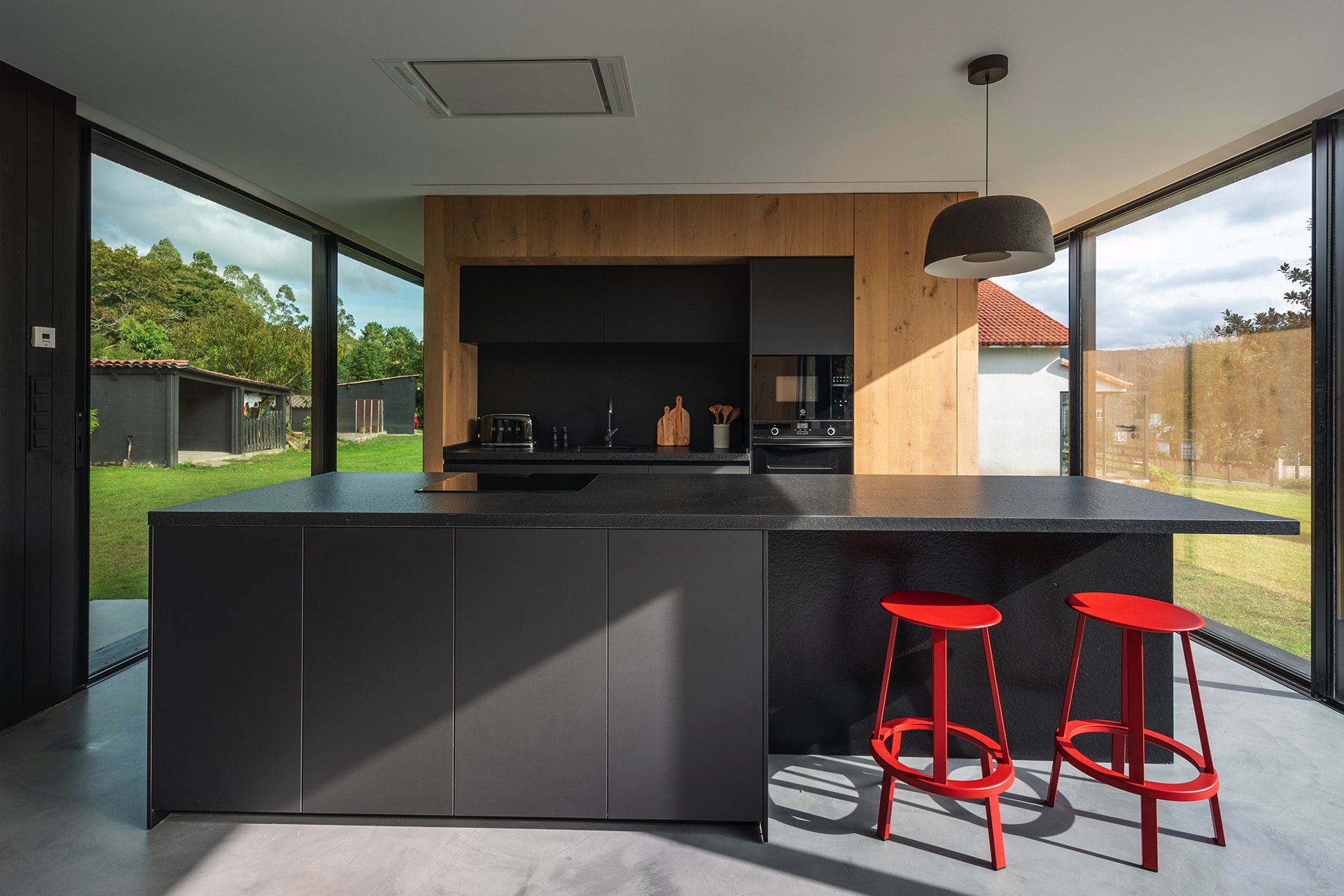 Cocina negra y madera con isla y taburetes rojos