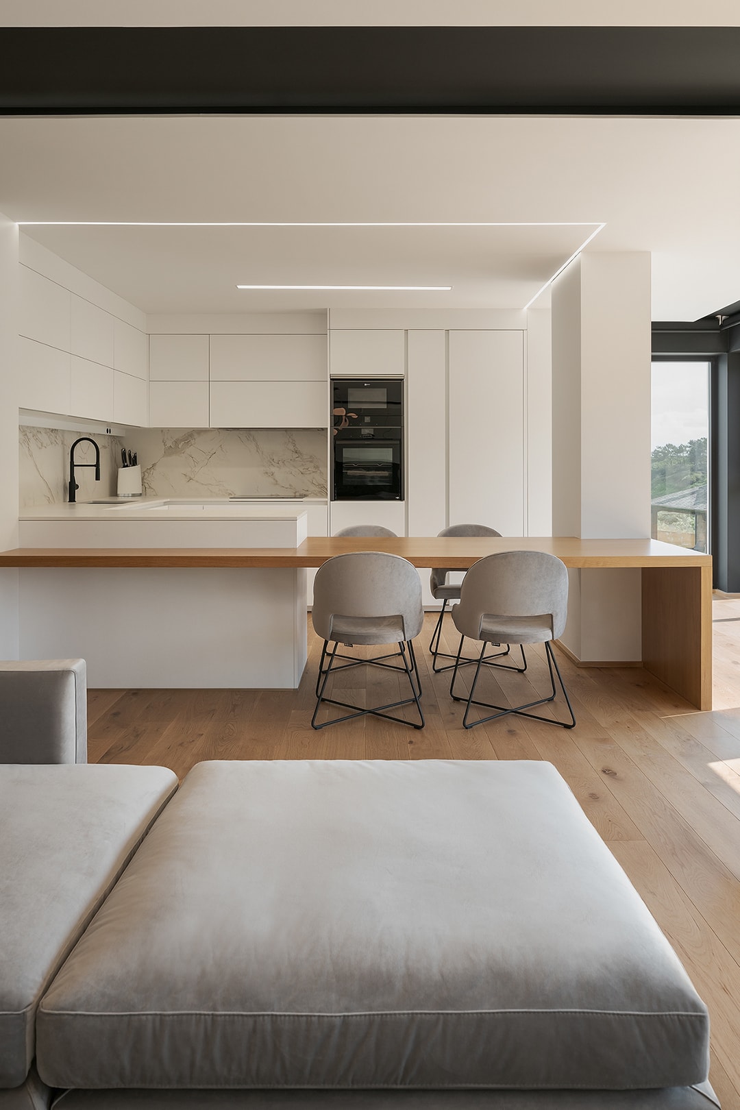 Cocina blanca Santos con barra de madera abierta al salón, en vivienda diseñada por Arnela Arquitectura.