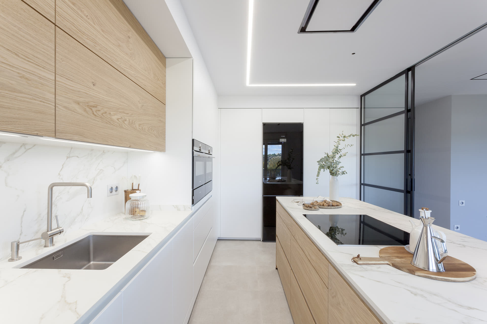 Cocina en blanco y madera de Santos con isla y cerramiento acristalado.