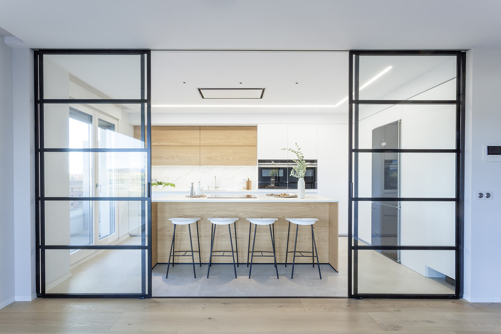 Cocina en blanco y madera con isla y cerramiento acristalado diseñada por Santos.