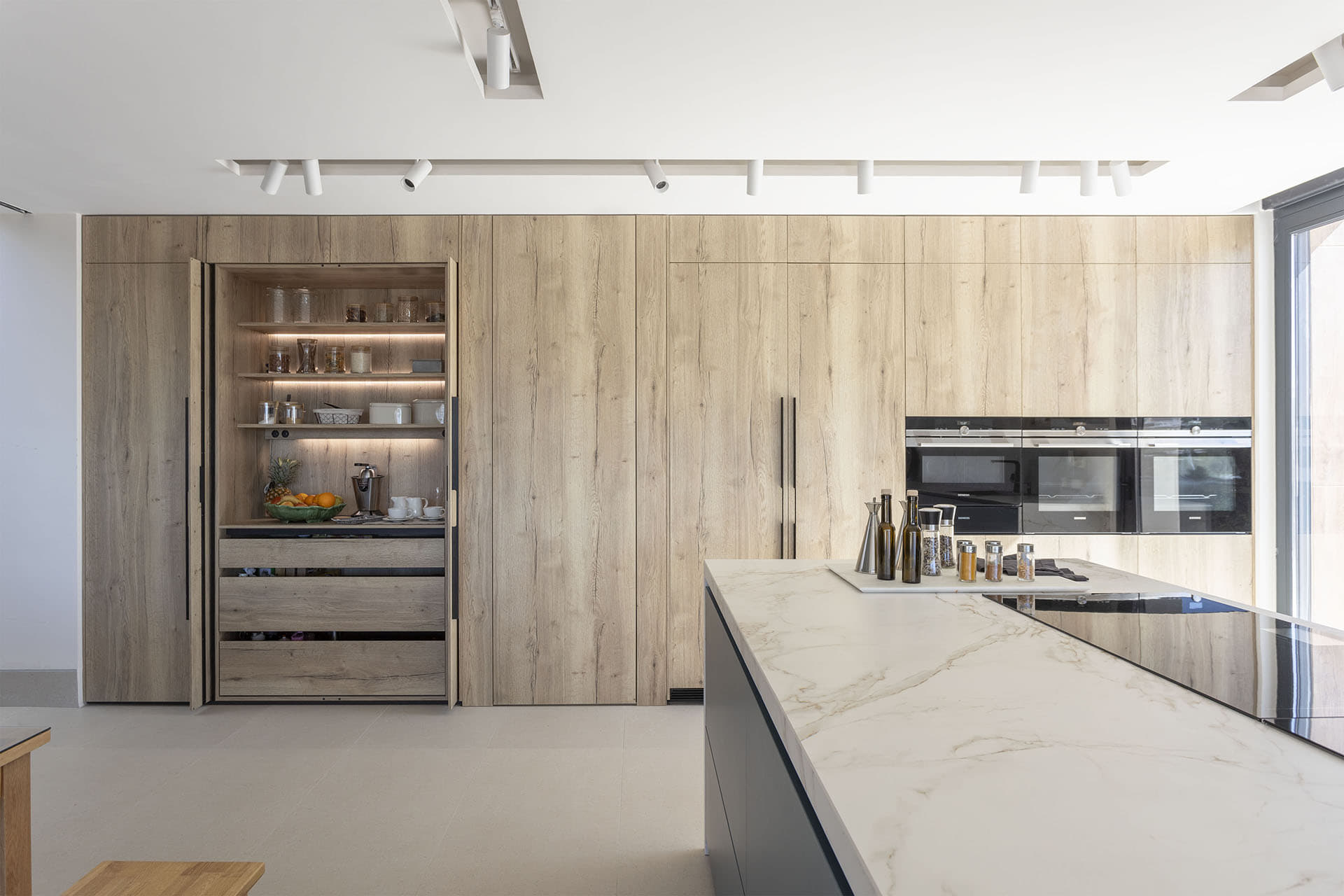 Cocina Santos con isla abierta al salón y muebles de almacenaje en madera.