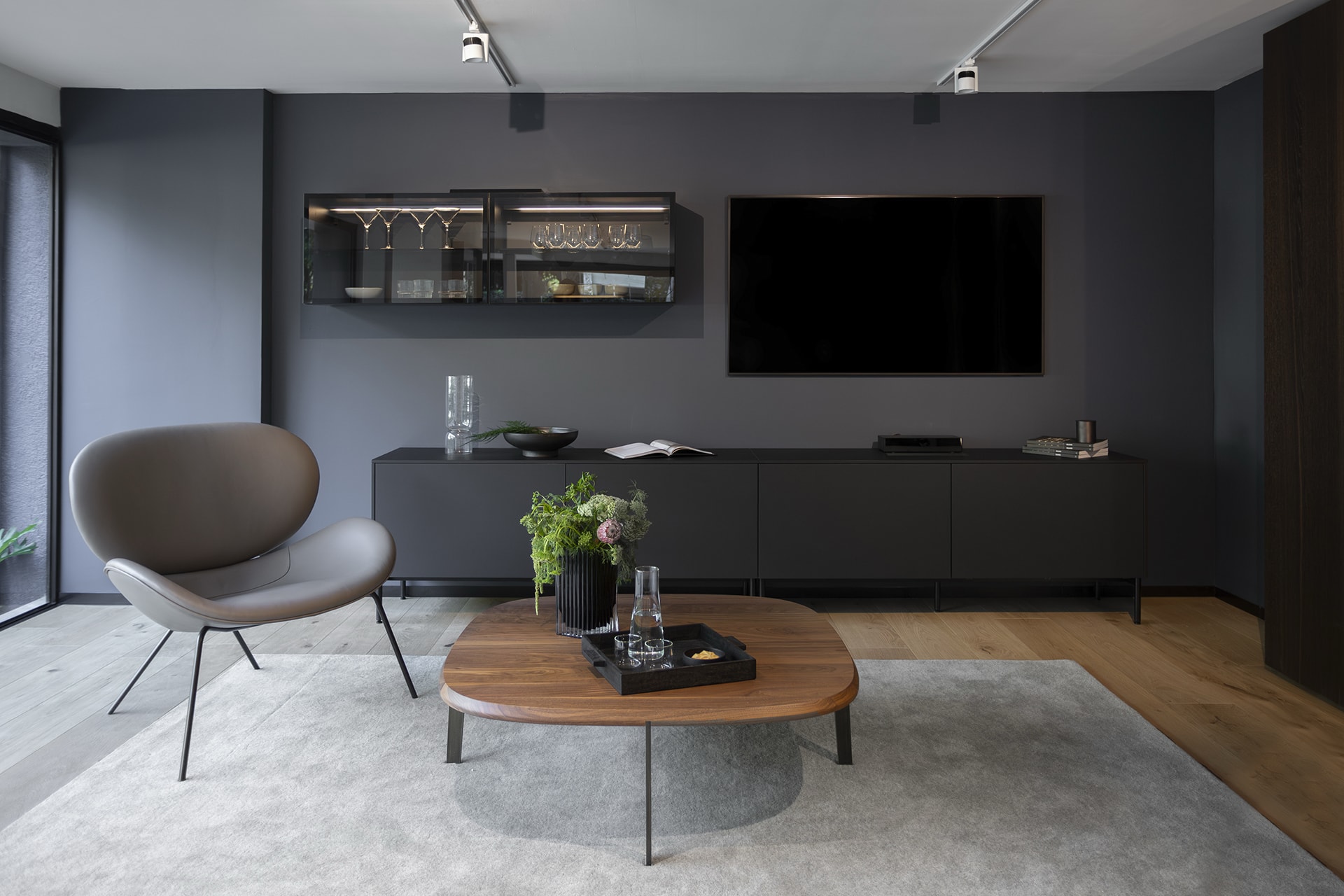 Woonkamer met geïntegreerde zwarte keuken met vitrinekasten met verlichting in de showroom van Santos keukens Mexico.
