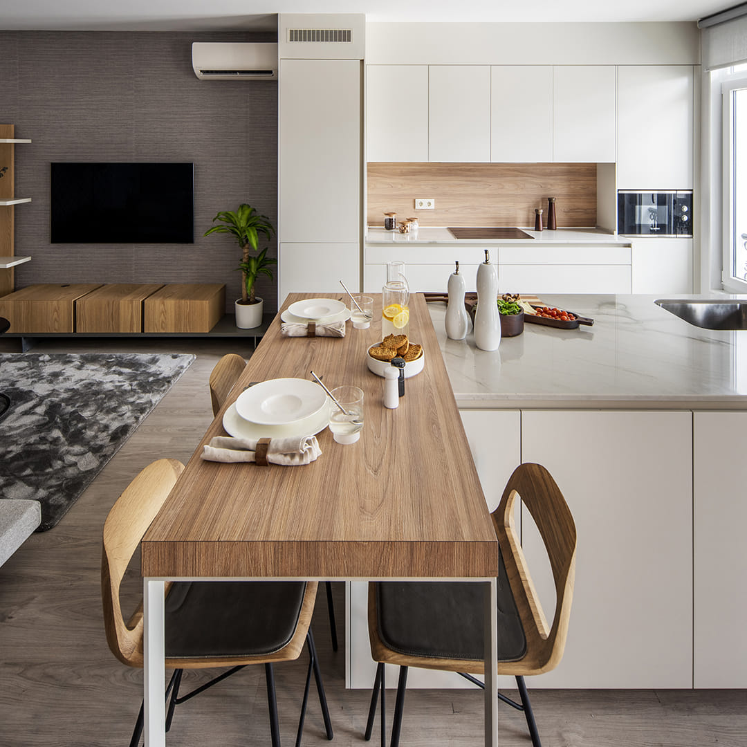 Cocina Santos blanca abierta al salón con península y barra de madera para desayunos.