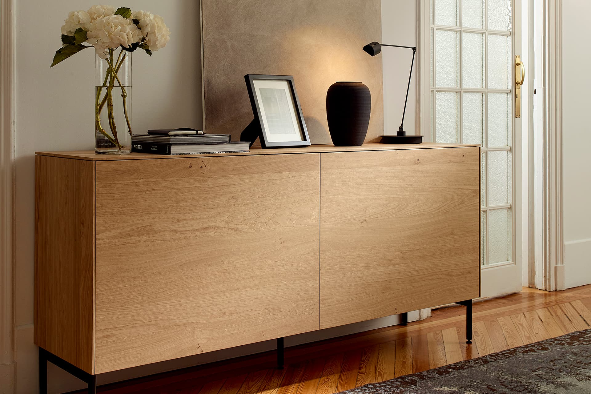 Mueble con estructura metálica lacada en negro, frentes lisos en acabado madera y dos módulos cajoneros con sistema de apertura asistida.