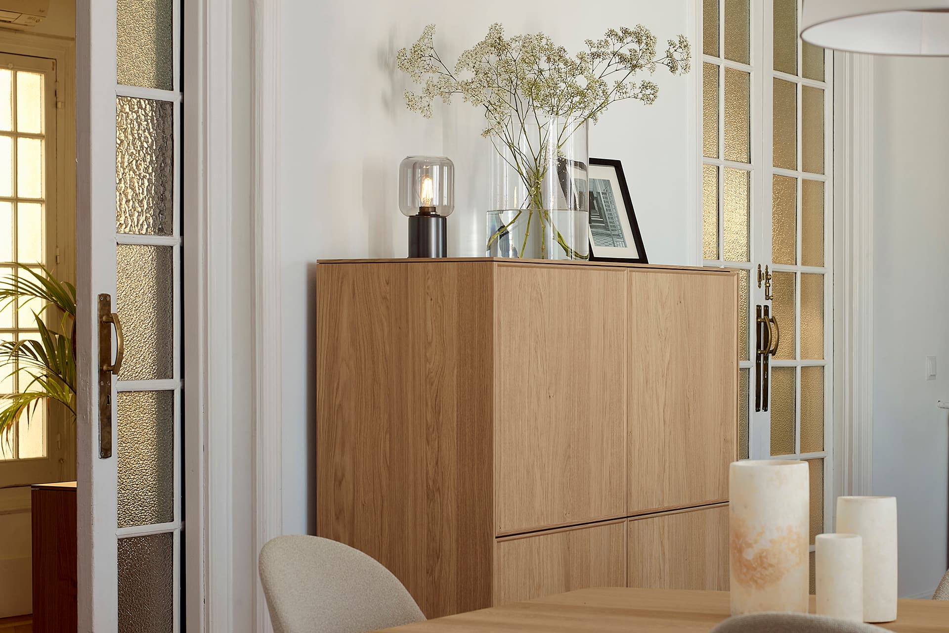 Composición con estructura metálica lacada en negro, frentes de chapa de madera natural perfilados en madera maciza, e interior con estantes y soporte para colgar copas.