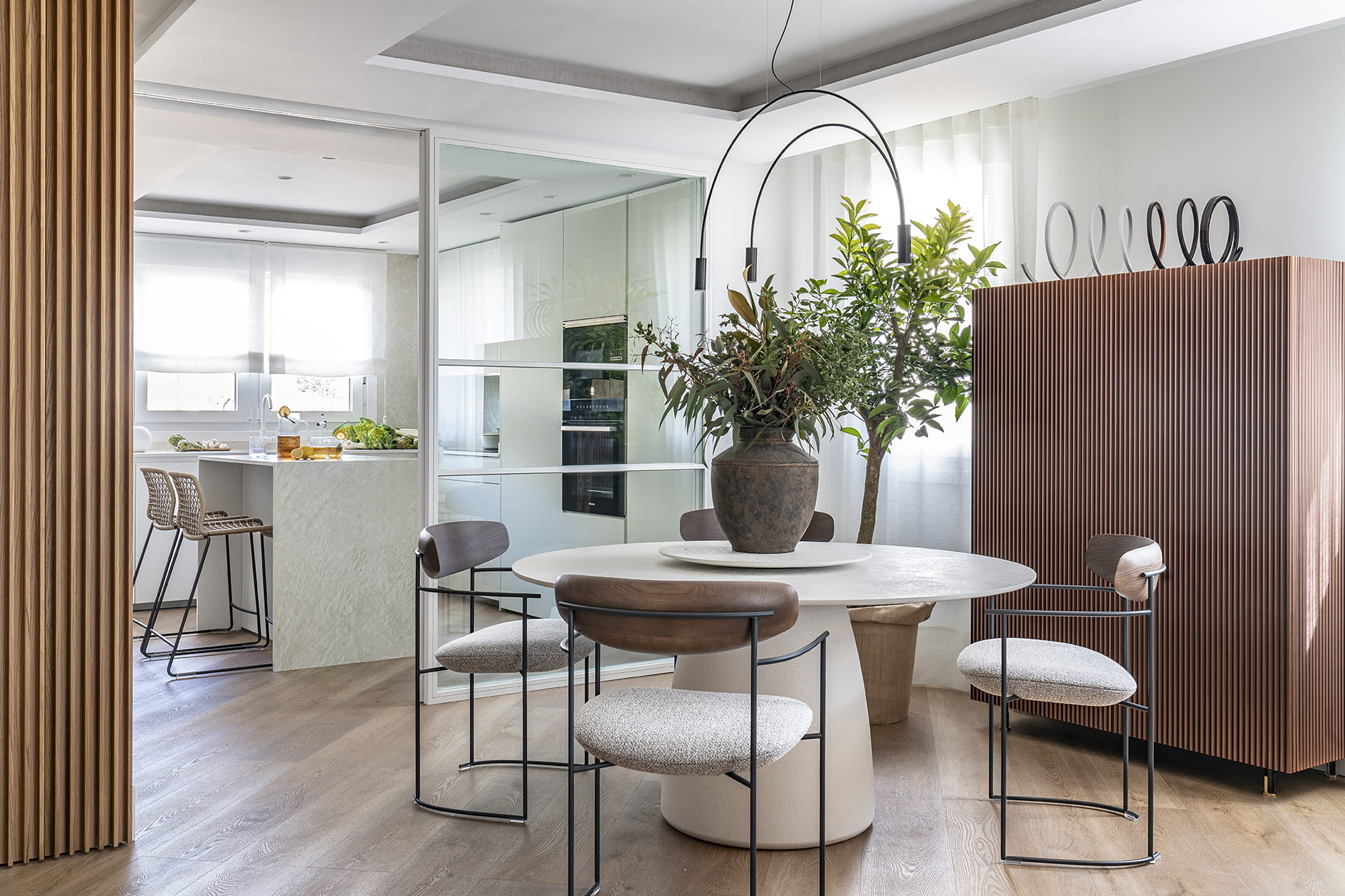 Cocina blanca con isla abierta al salón comedor con cerramiento de cristal diseñado por Santos.
