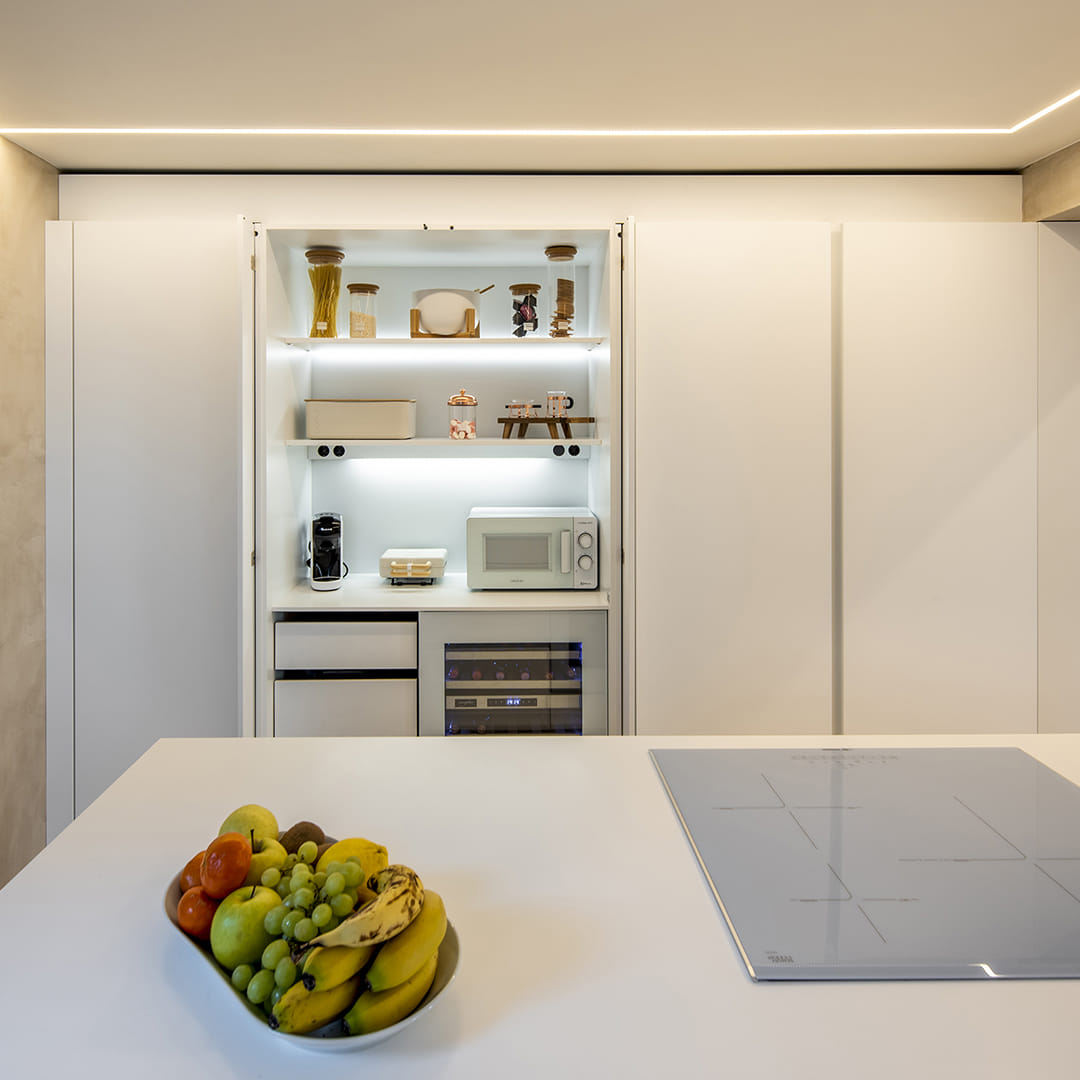 Armario con puertas escamoteables e iluminación interior abierto en una cocina blanca diseñada por Cocinas Santos.