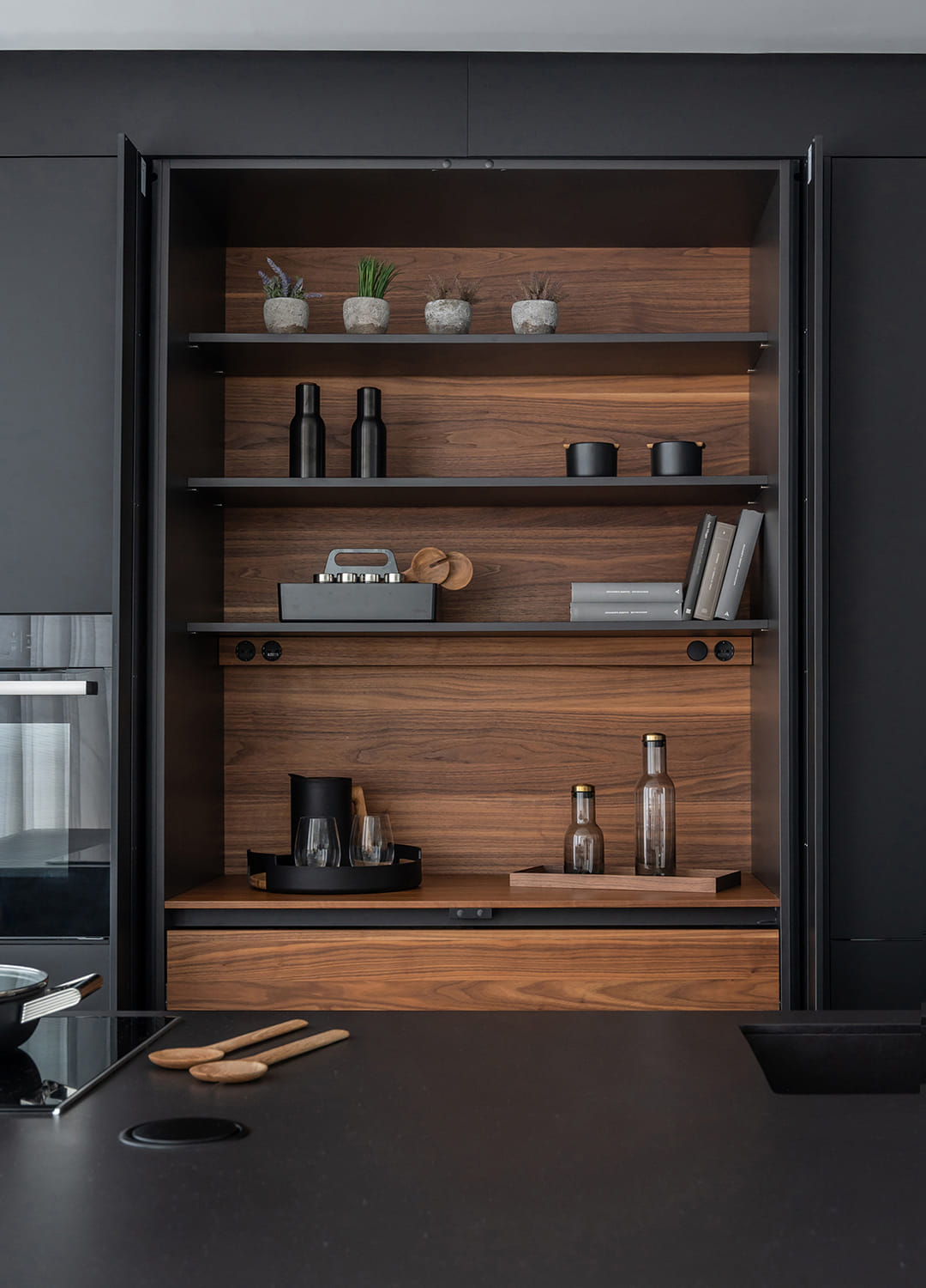 Armario con puertas escamoteables y perfil de iluminación en una cocina negra de Santos.