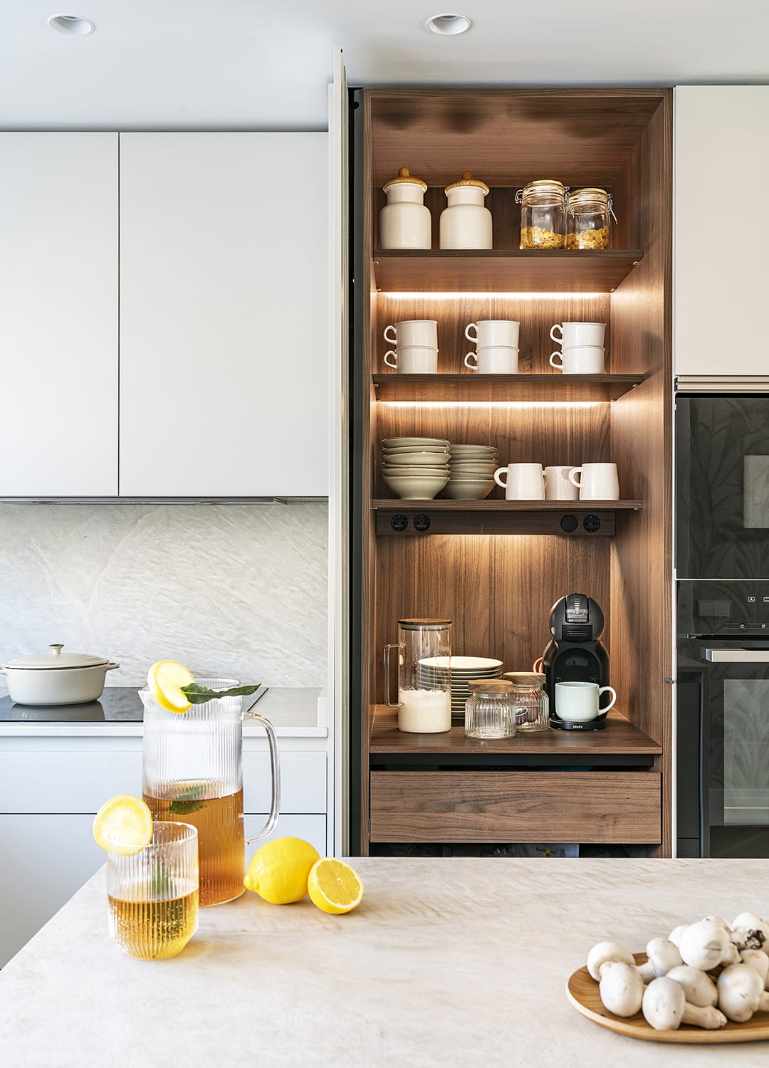 Armario con puertas escamoteables e iluminación interior en una cocina blanca de Santos.