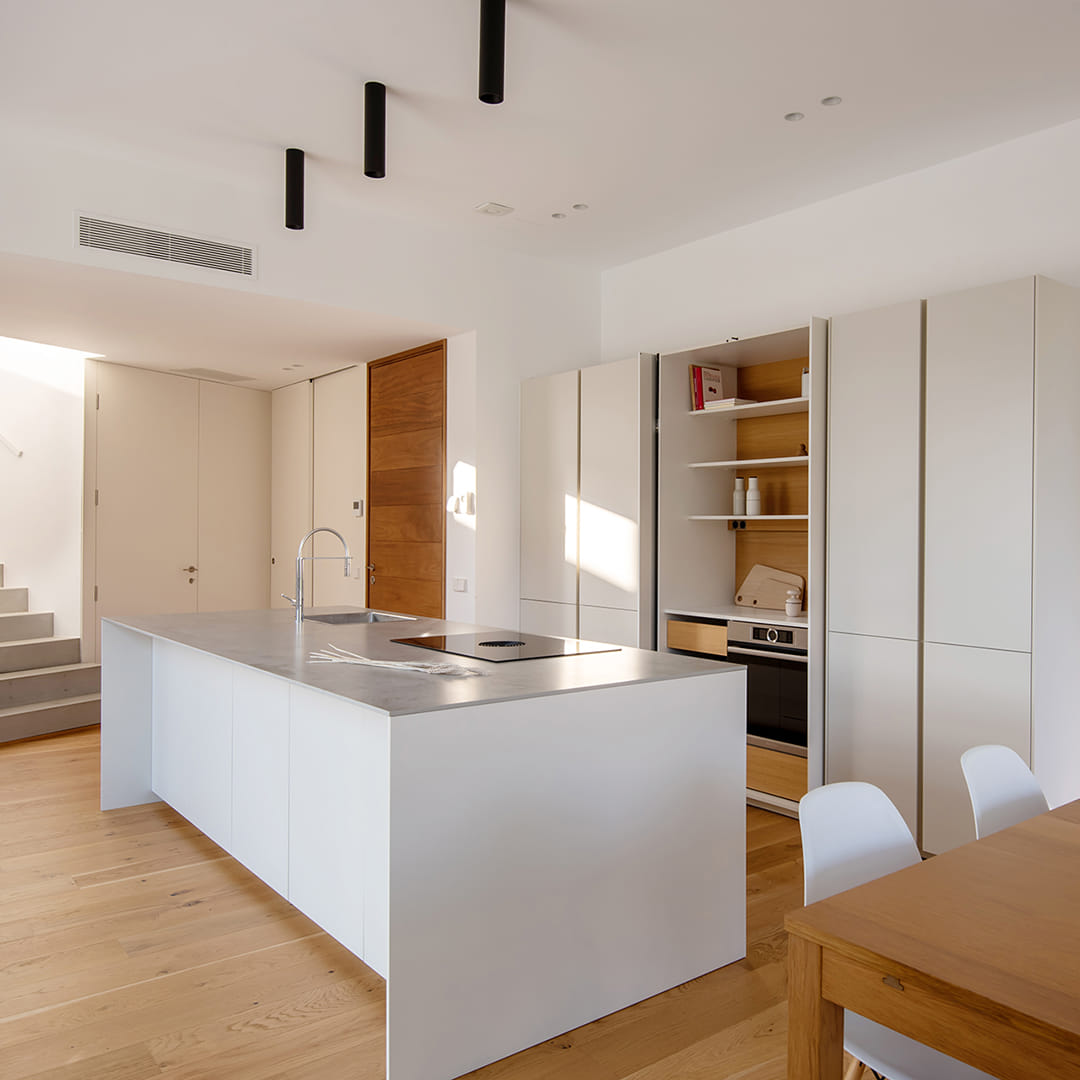 Cocina blanca Santos con isla y armarios con puertas escamoteables.