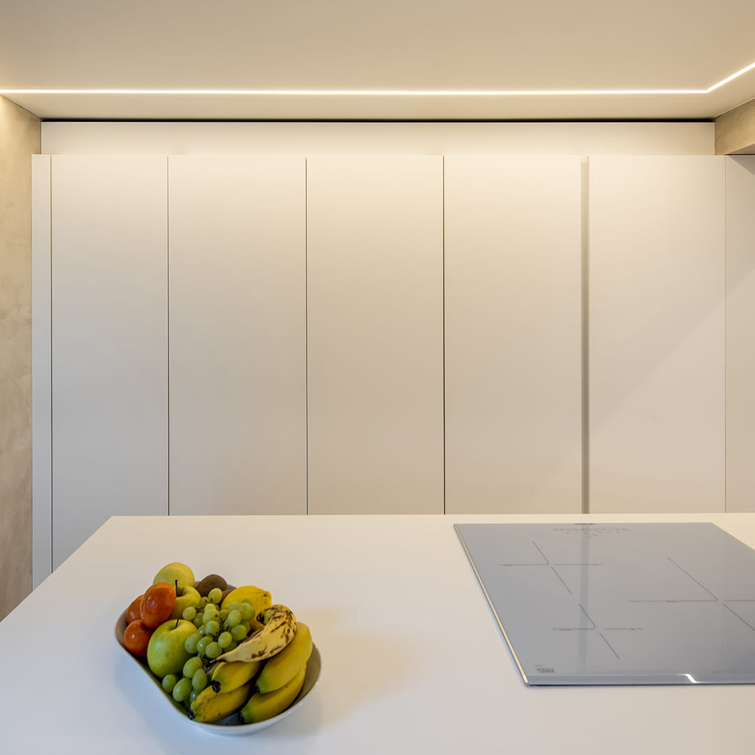 Detalle de isla de cocina y armarios con puertas escamoteables en una cocina blanca de Santos.