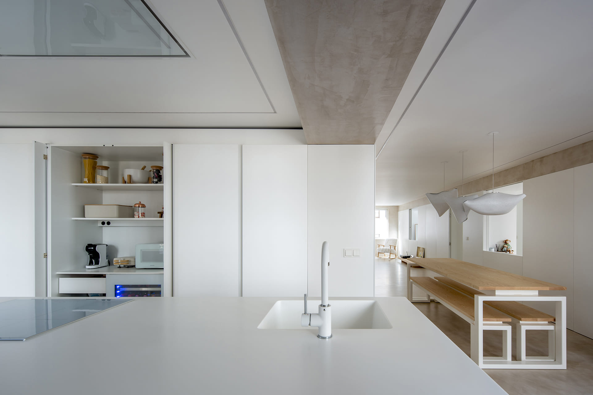 Zona de fregadero en una cocina blanca con isla y armarios con puertas escamoteables de Santos.