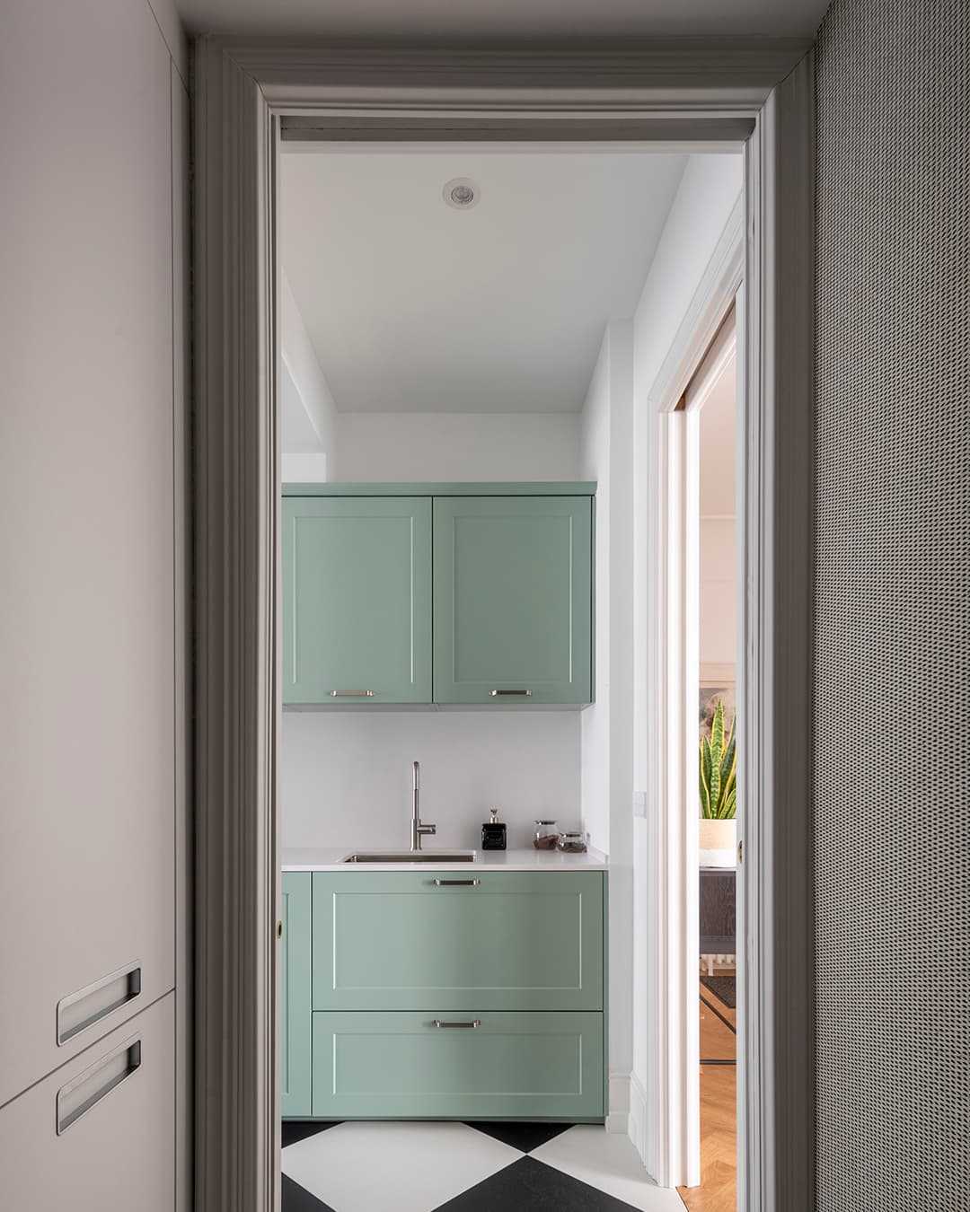 View of the kitchen cabinets and sink in a green kitchen by Santos Kitchens.