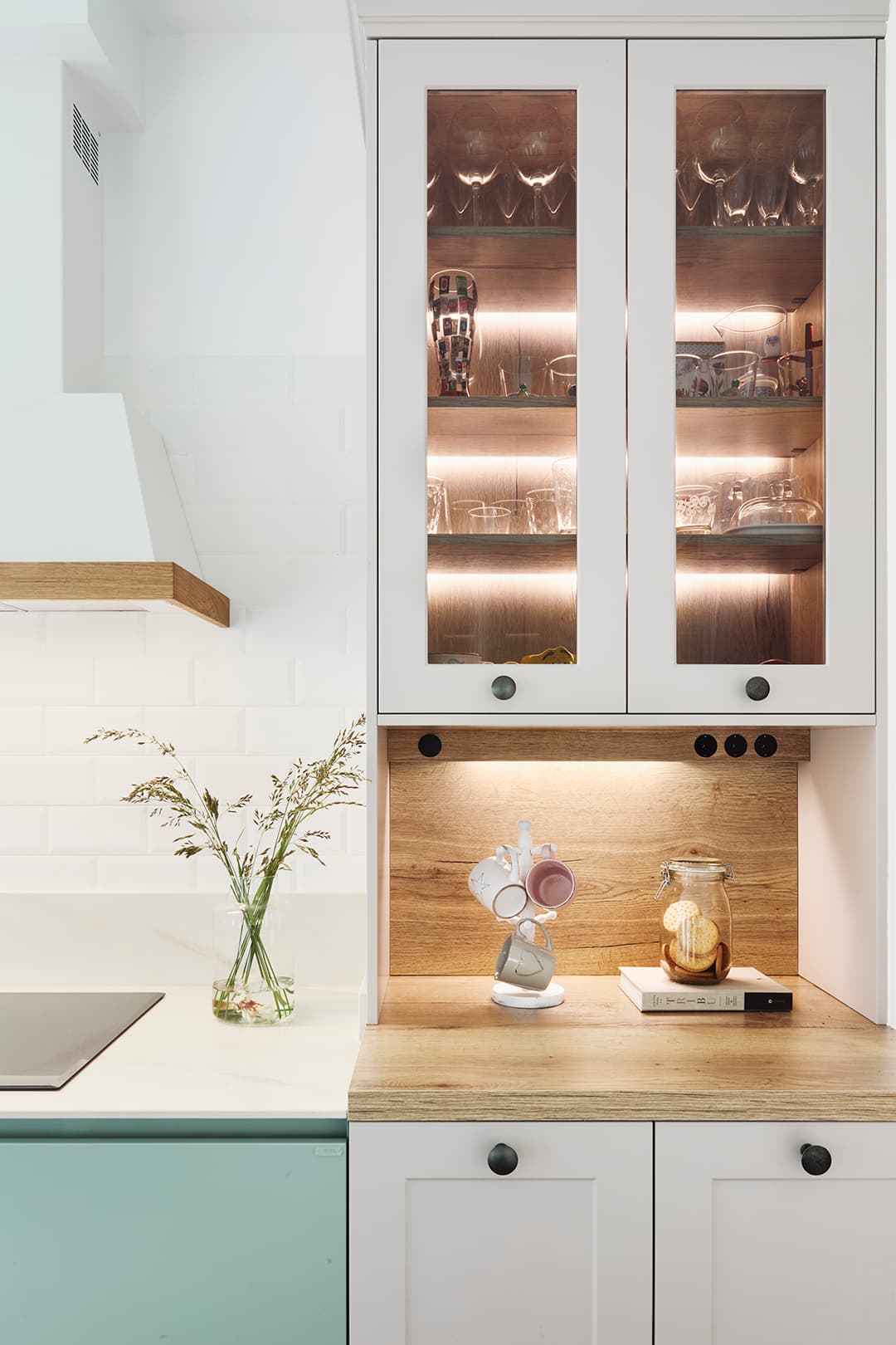 Kitchen glass door unit with interior lighting and wooden finishes in a green kitchen by Santos Kitchens.