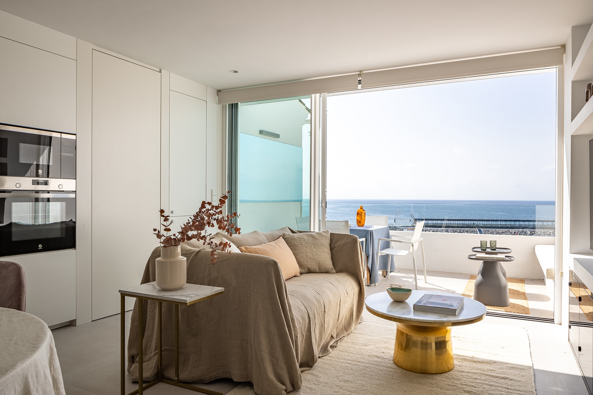 Salón y terraza de una vivienda con una cocina blanca diseñada por Santos.