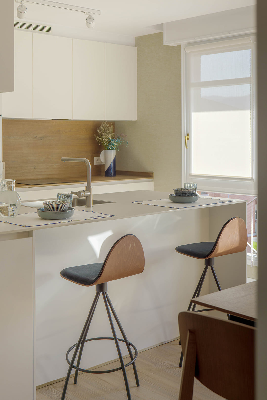 Cocina blanca con península y taburetes diseñada por Santos.