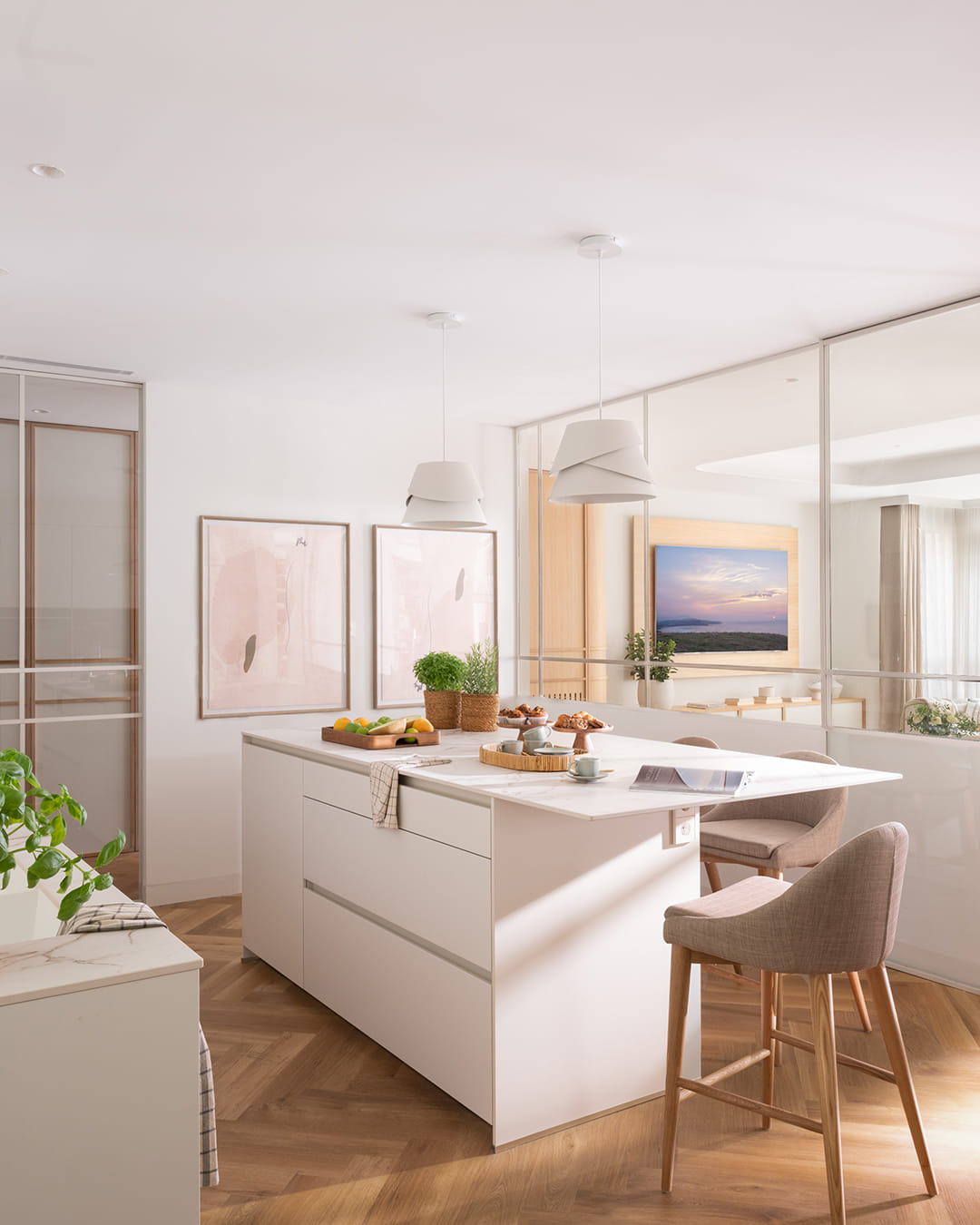 Isla de cocina con taburetes en una cocina blanca abierta al salón.