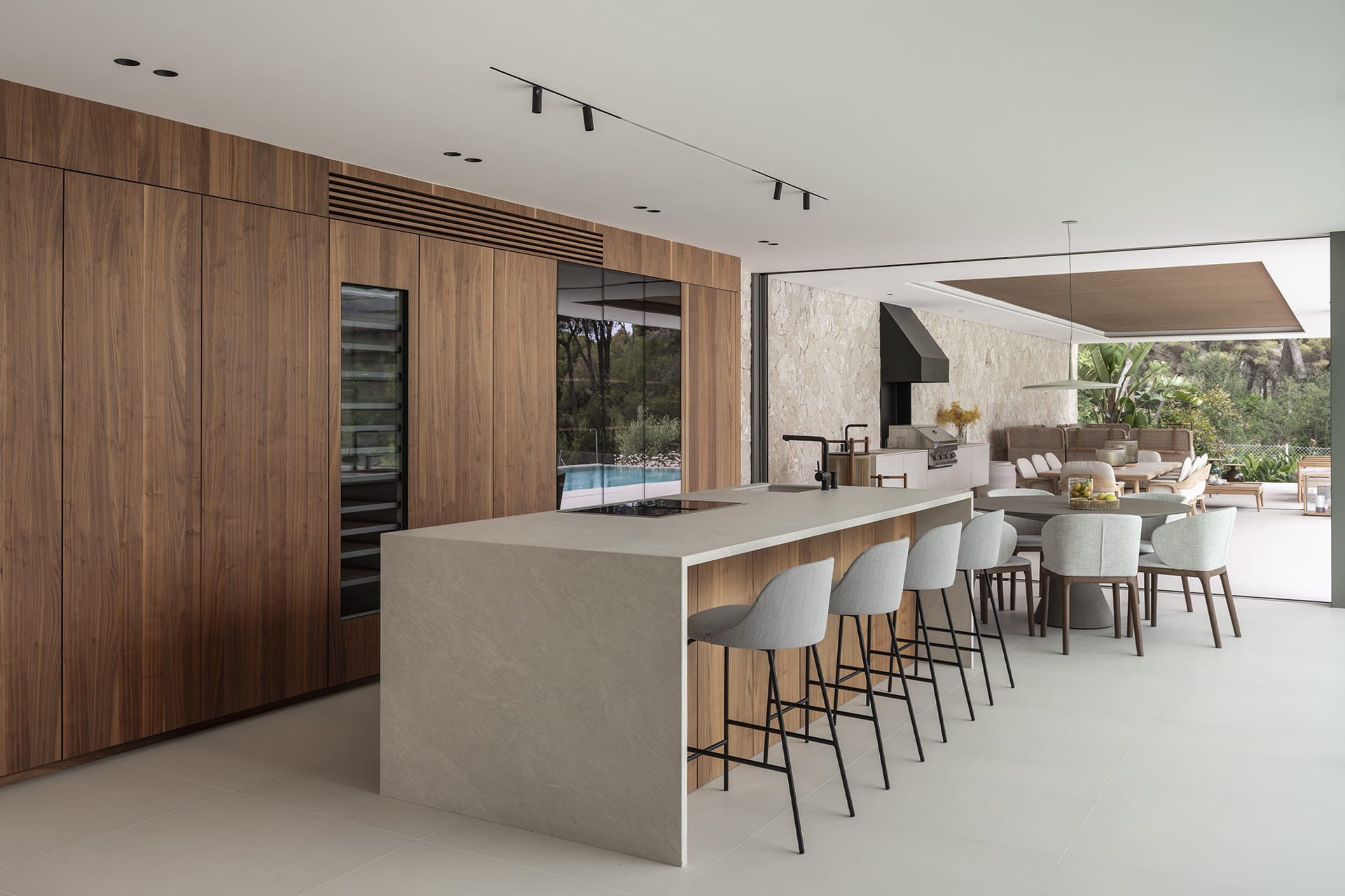 Cocina blanca y madera con isla y taburetes abierta al comedor y exterior.