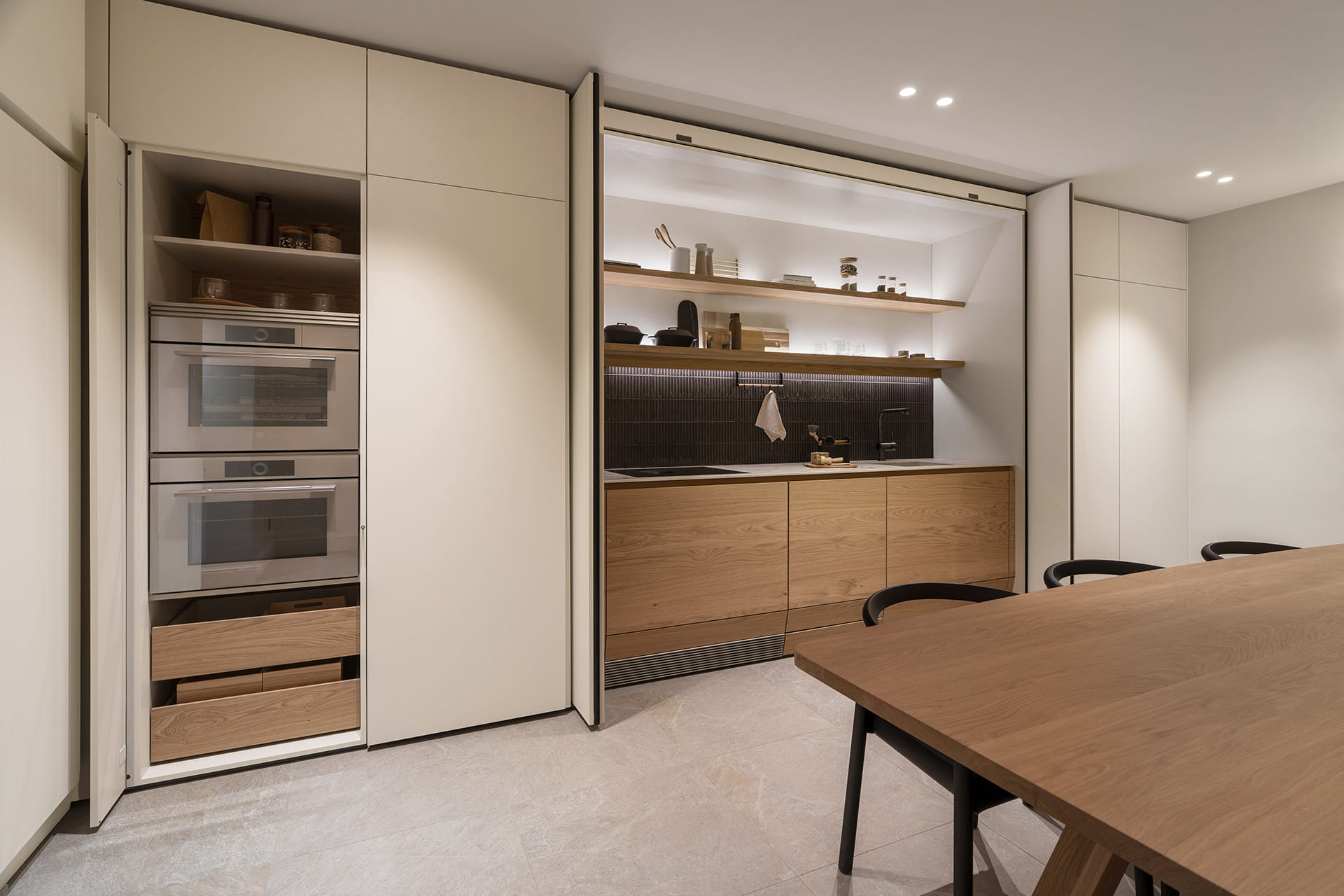 Cocina lineal oculta tras puertas escamoteables con electrodomésticos integrados en el showroom de Cocinas Santos en Suiza.