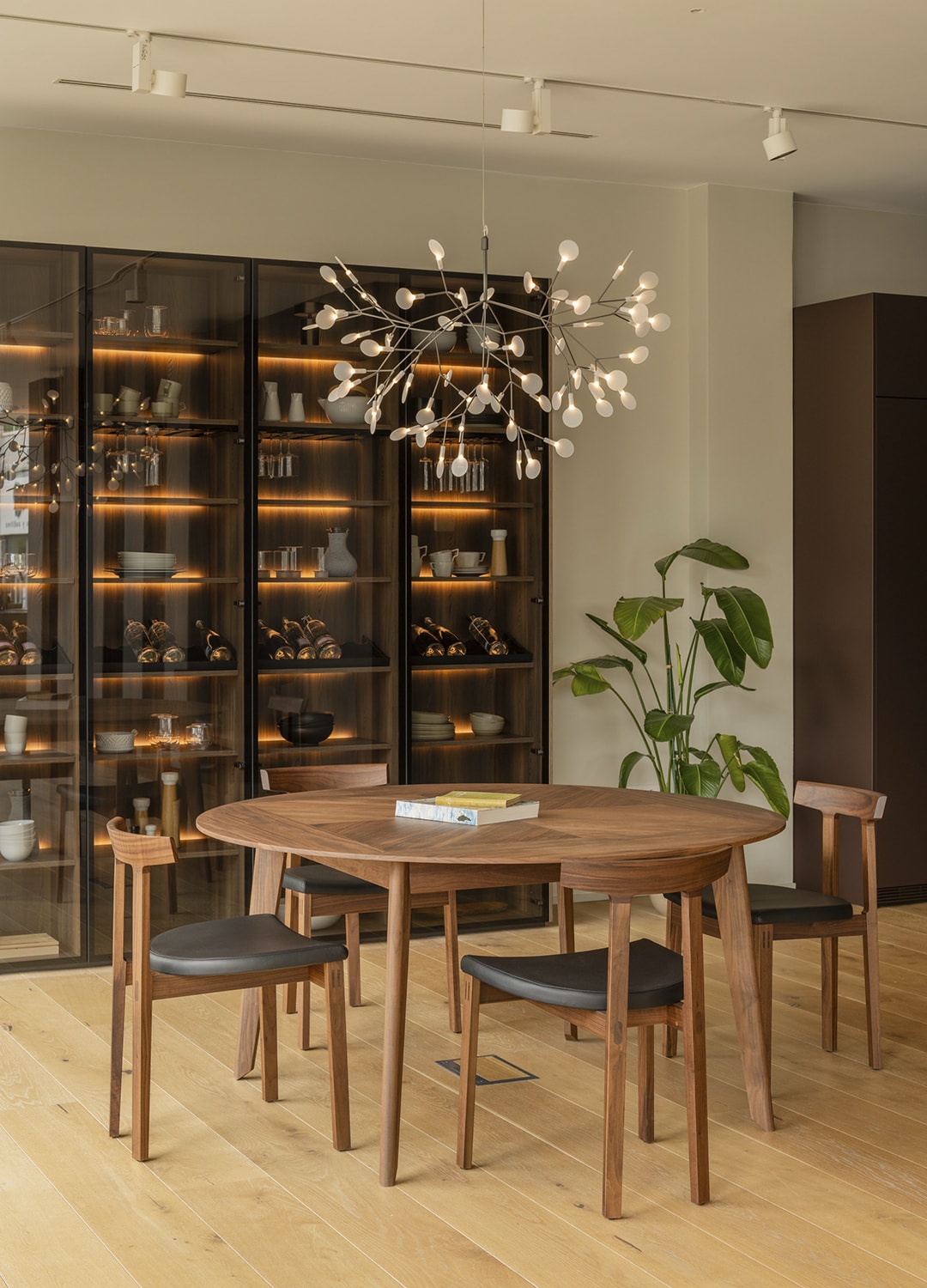 Mesa de comedor y vitrina con iluminación interior en la nueva exposición de Cocinas Santos en Santiago.